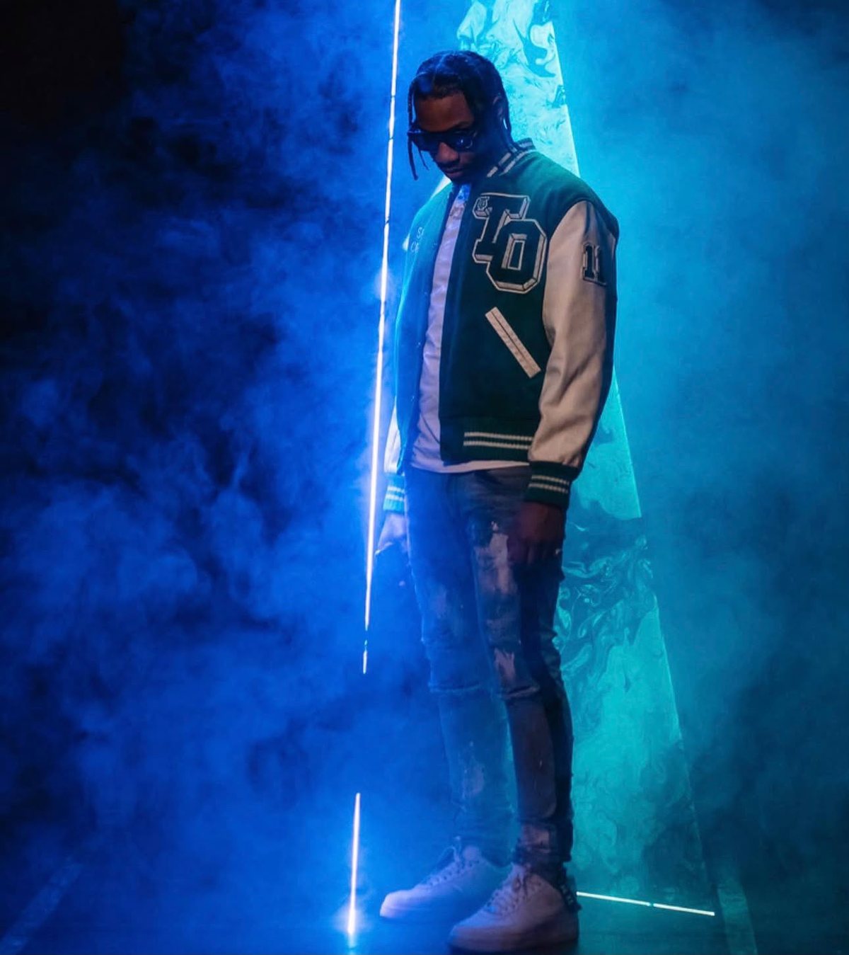 Vulture in a green varsity jacket, lit by a single hard blue light through smoke.